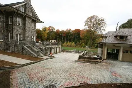 Stone courtyard between two rustic buildings, with autumn trees in the background.