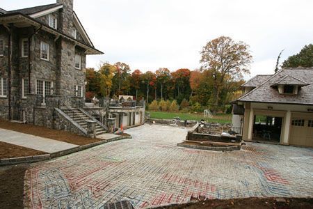 Abandoned stone courtyard with two buildings, a paved path, and autumn trees in the background