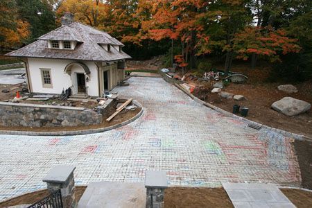 Stone-paved driveway curving past a small white cottage with autumn trees and landscaping stones