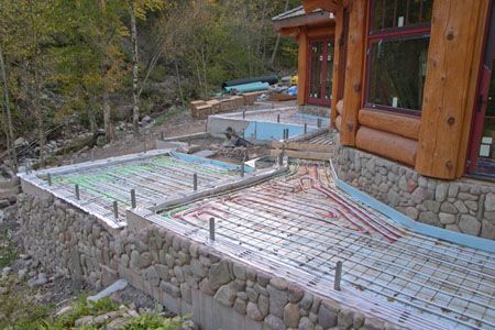Wooden house patio under construction with rebar mesh and stone retaining wall on a hillside