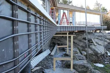 Construction site with metal deck framing, red ladder, and temporary supports over rocky ground