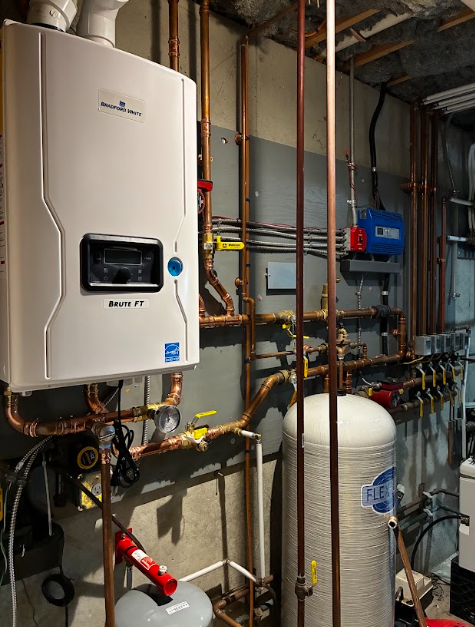 Boiler room with white water heater, blue pump, pipes, and pressure tank against unfinished walls.