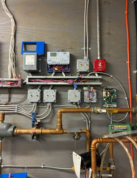 Wall-mounted utility meters, switches, and copper pipes in a mechanical room