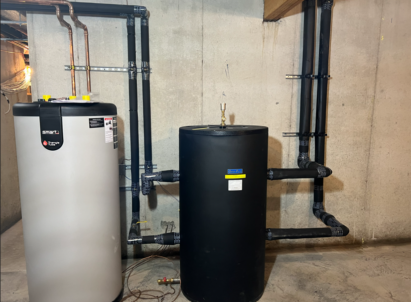 Two water heaters with black piping in a basement utility room.