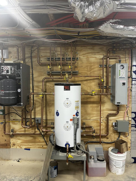 Basement utility room with a white water heater, exposed pipes, ductwork, and electrical panels