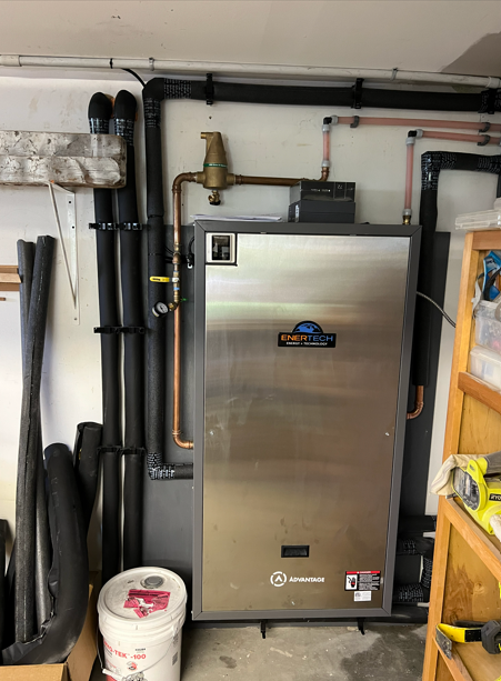 Stainless steel mechanical unit with pipes and hoses in a utility room, beside a white bucket and shelving