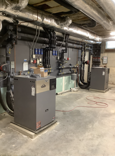 Industrial mechanical room with HVAC equipment, pipes, and ductwork on a concrete floor