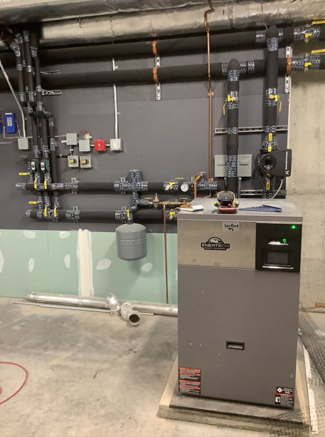 Boiler room equipment with pipes, valves, and a gray HVAC unit in front of a frosted glass barrier