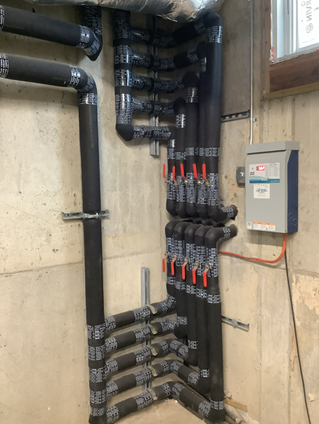 Electrical and plumbing pipes with red valves in a utility room beside a gray control box