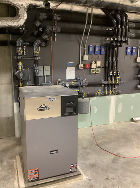 Industrial basement with large gray equipment unit, exposed pipes, and wall-mounted electrical controls