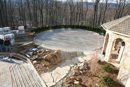 Backyard stone patio under construction beside a gazebo, with wooded hillside in the background