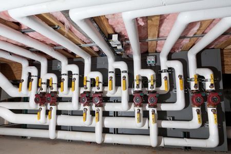 Plumbing manifold with multiple white pipes, valves, and gauges installed under a floor or ceiling.