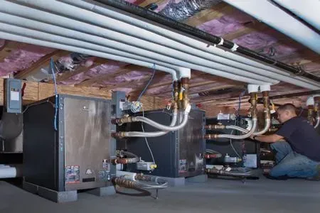 Technician inspecting HVAC equipment and ductwork in a basement crawlspace