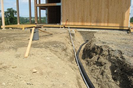 Construction site with a wooden building, trench, and black utility pipe running through dirt.