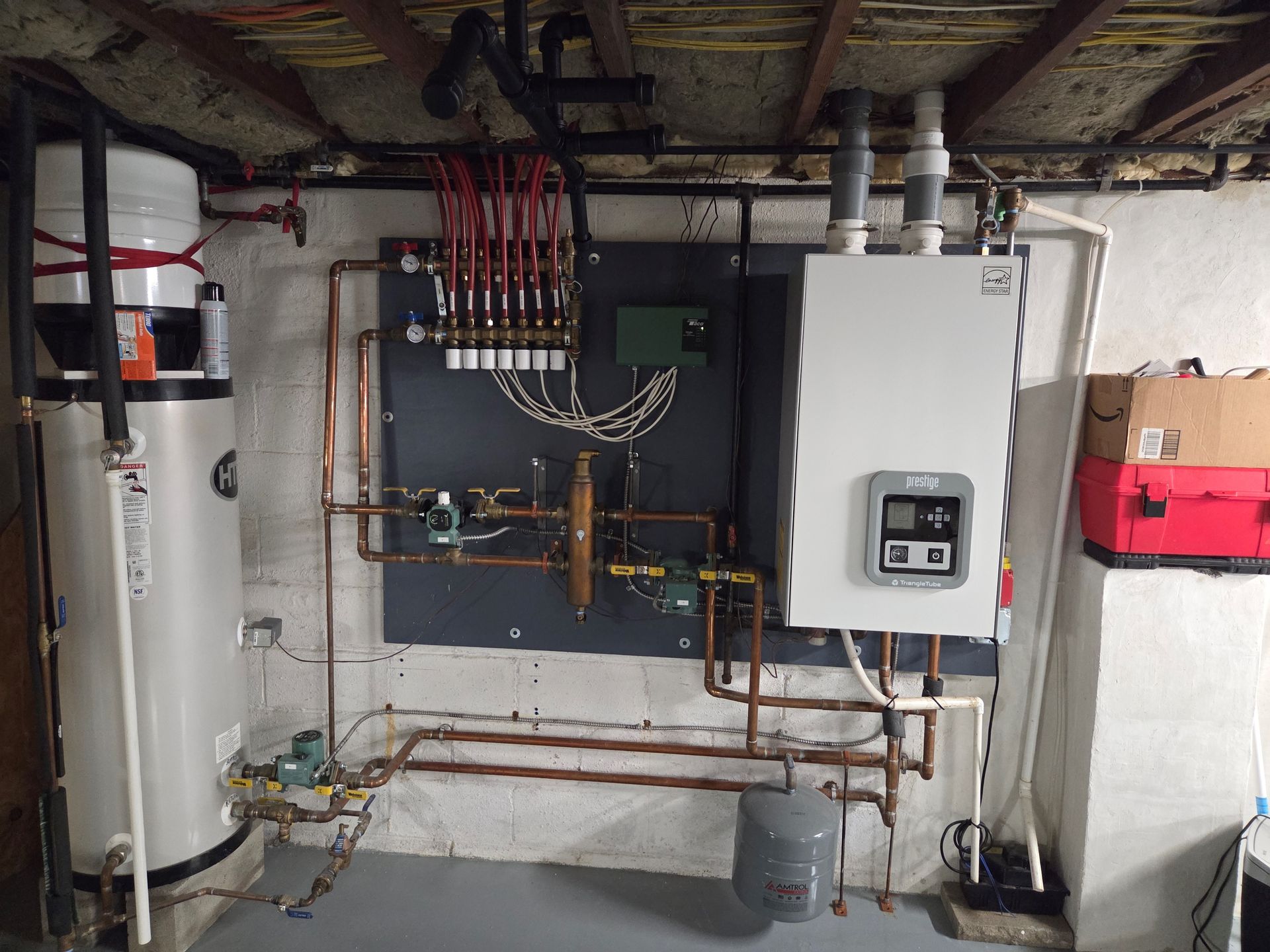 Basement utility room with water heater, electrical panels, piping, and red toolbox on the wall