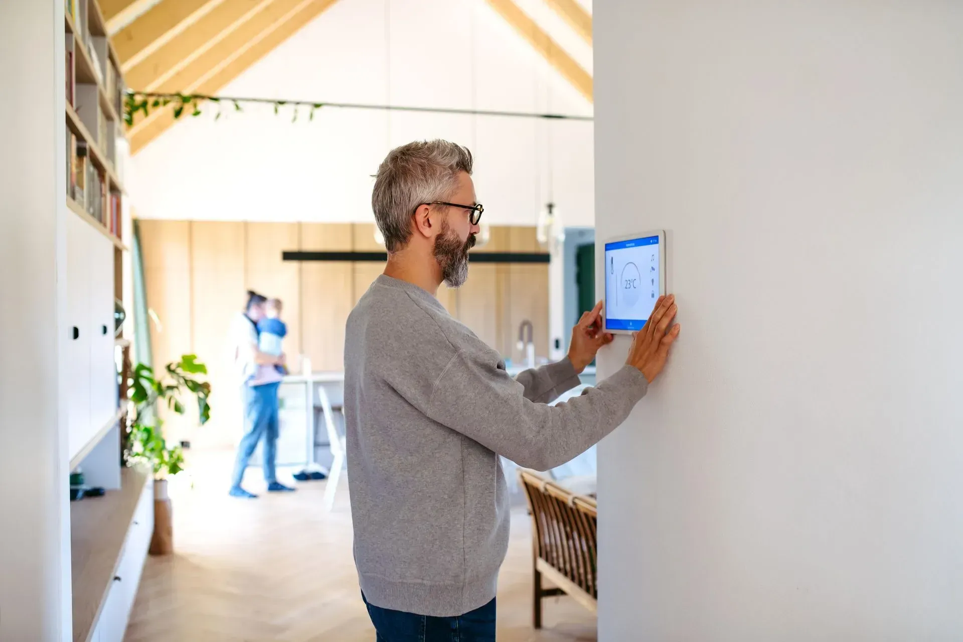 Man using a tablet mounted on a wall in a bright hallway, with another person blurred in the background