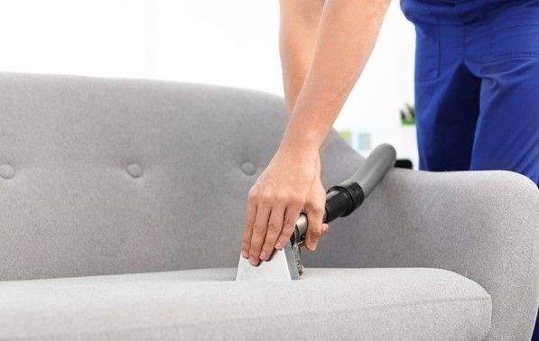 Person vacuuming a gray sofa with a handheld upholstery attachment.