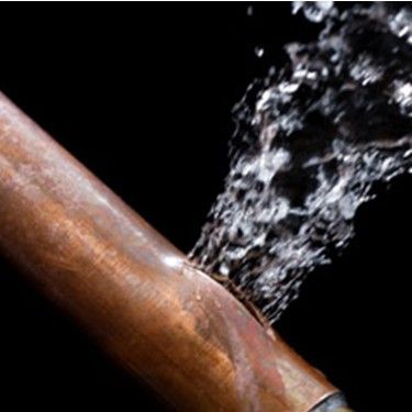 Burst copper pipe spewing water against a black background.