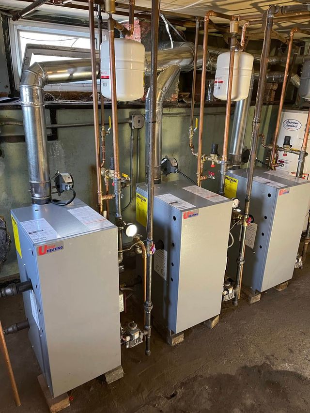 Three white HVAC/furnace units with copper pipes and ductwork in a utility basement room