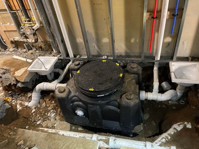Underground black septic tank with pipes and valves in a dirt utility trench