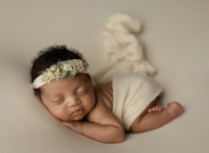 A newborn baby girl wearing a headband is sleeping on a blanket.