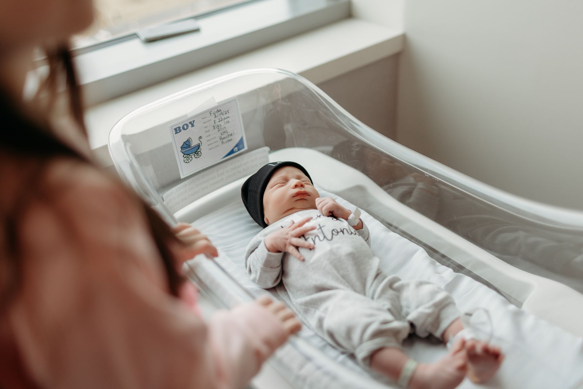 A little girl is looking at a newborn baby in a hospital crib.