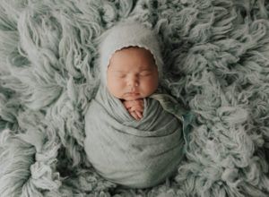 A newborn baby is wrapped in a blanket and wearing a hat.