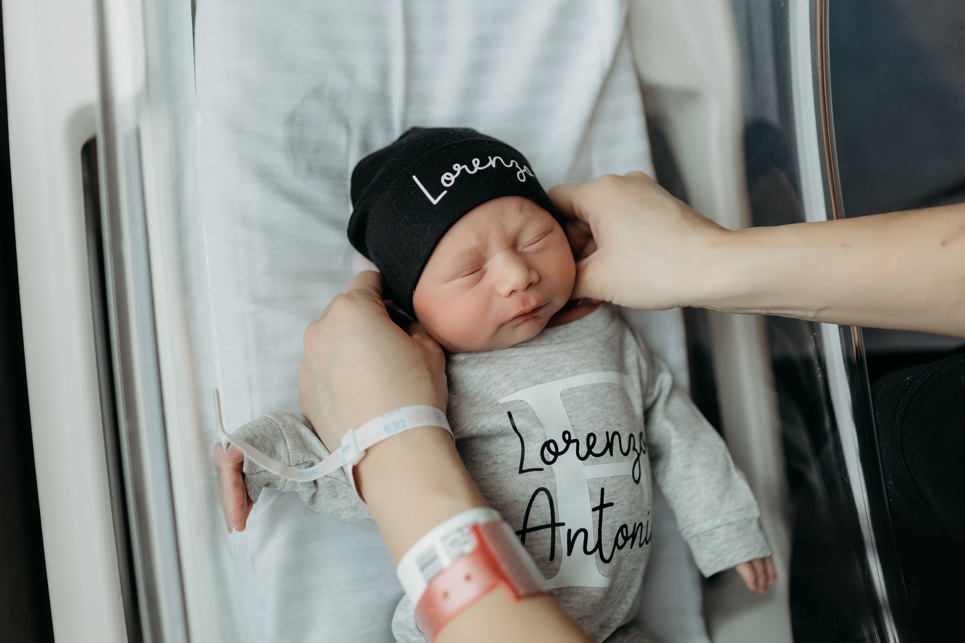 A woman is putting a hat on a newborn baby in a hospital bed.