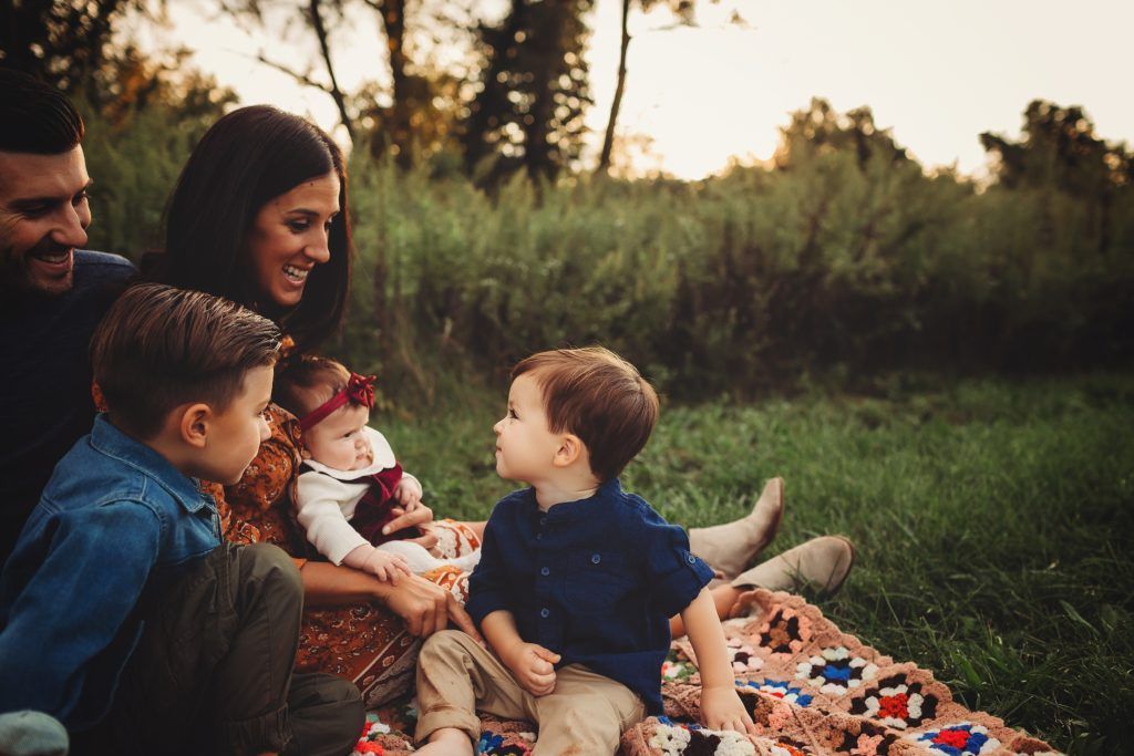 A family is sitting on a blanket in the grass.
