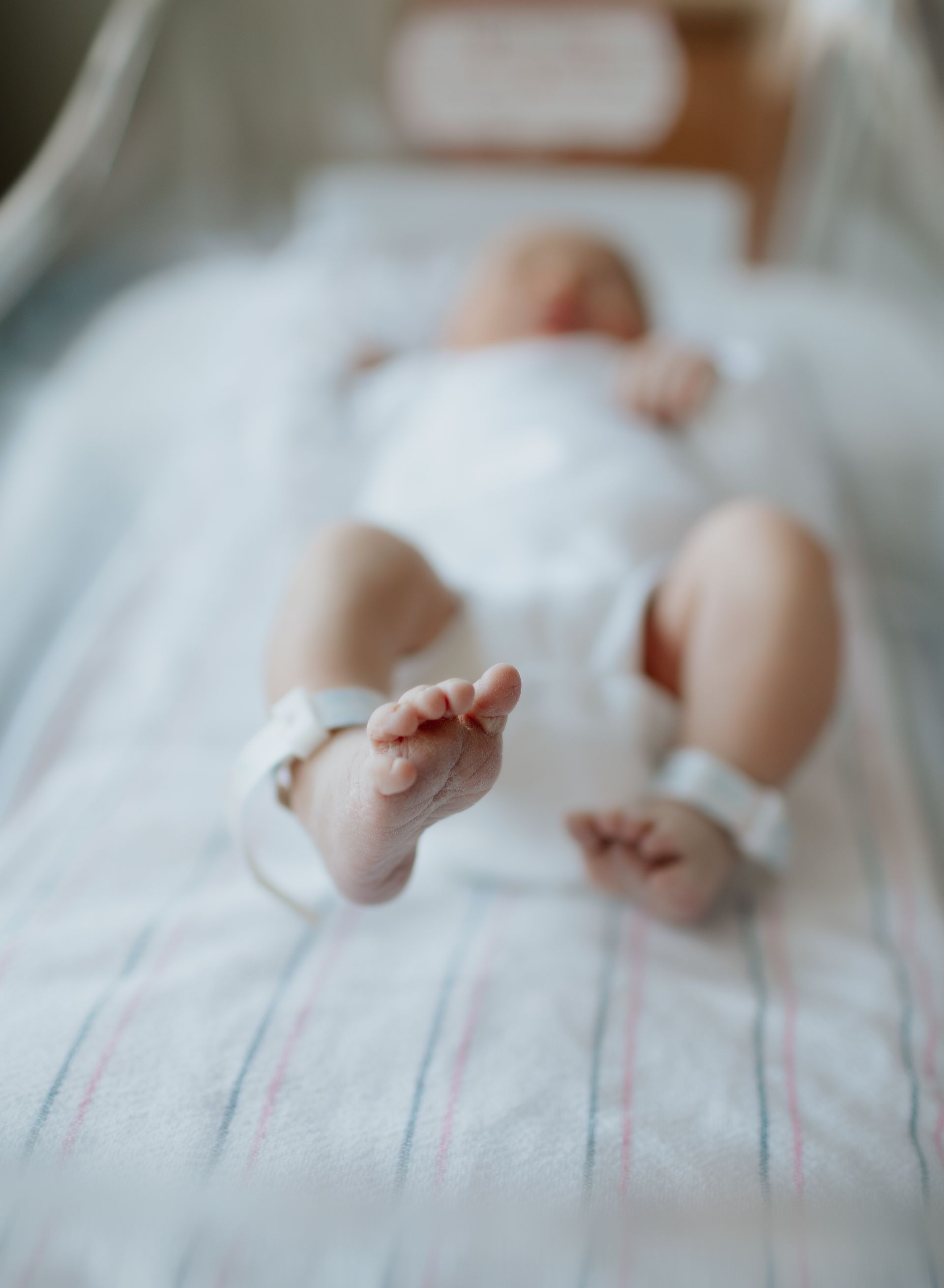 Newborn baby lying in a hospital crib, feet in focus with identification bands.