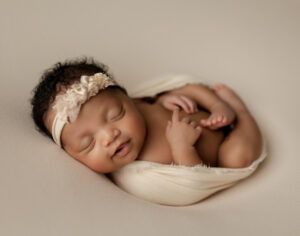 A newborn baby is wrapped in a white blanket and wearing a headband.