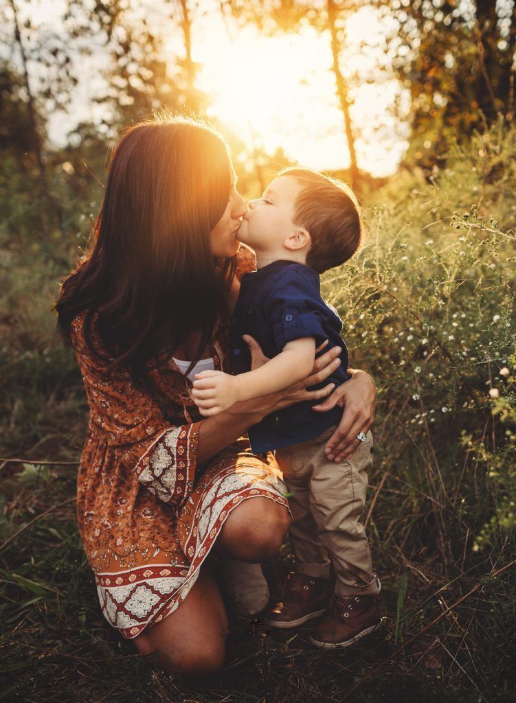 A woman is kissing her son on the cheek in a field.