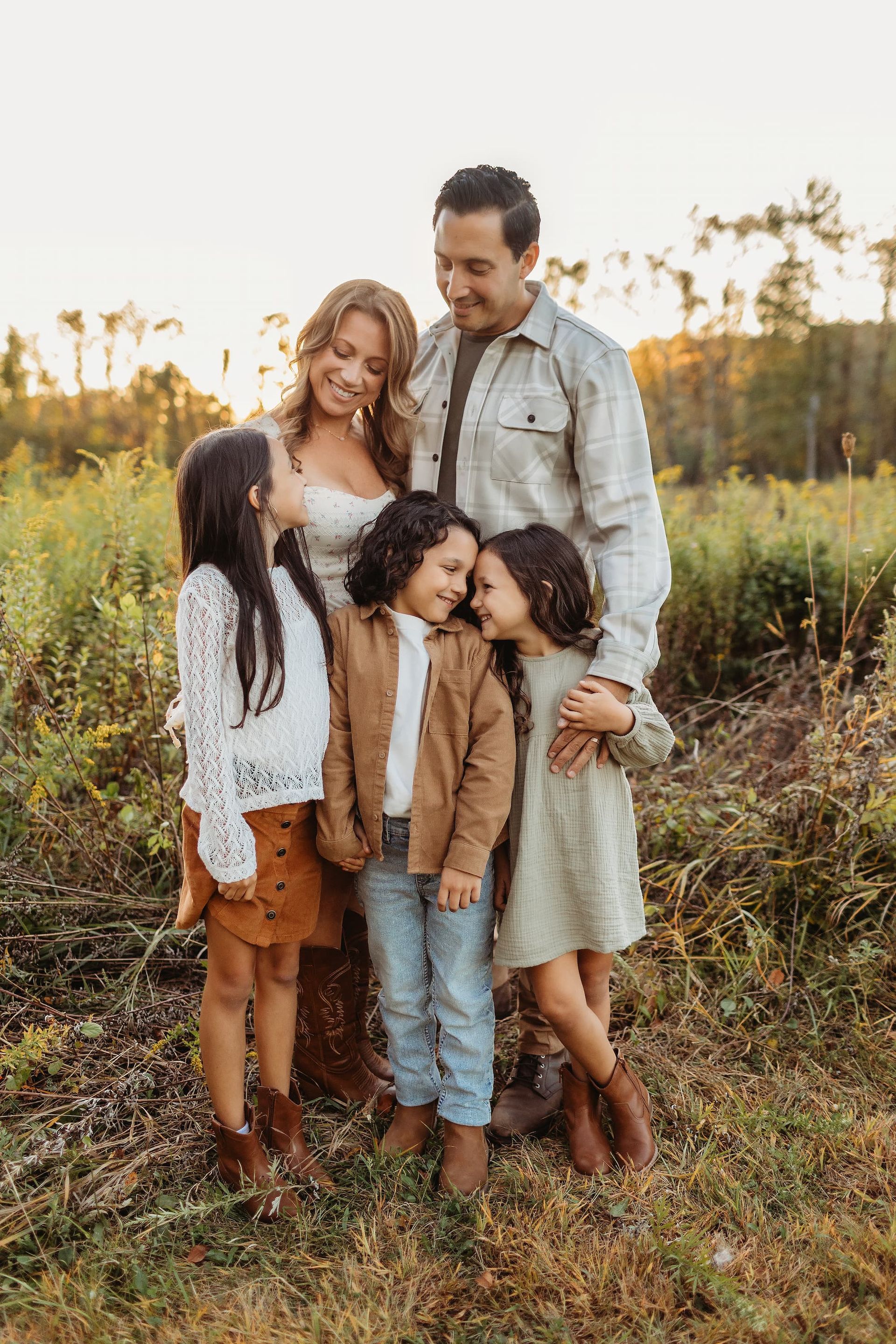 Family of five embraces in a field, golden hour lighting. Two girls and a boy stand in front.