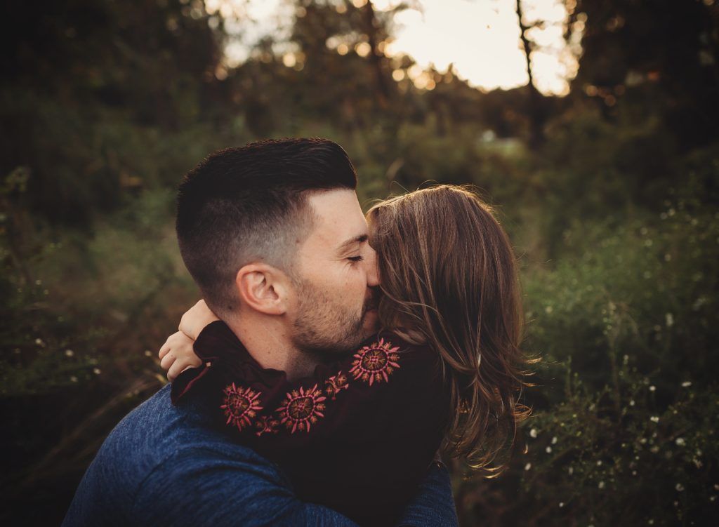 A man is kissing his daughter on the cheek in a field.