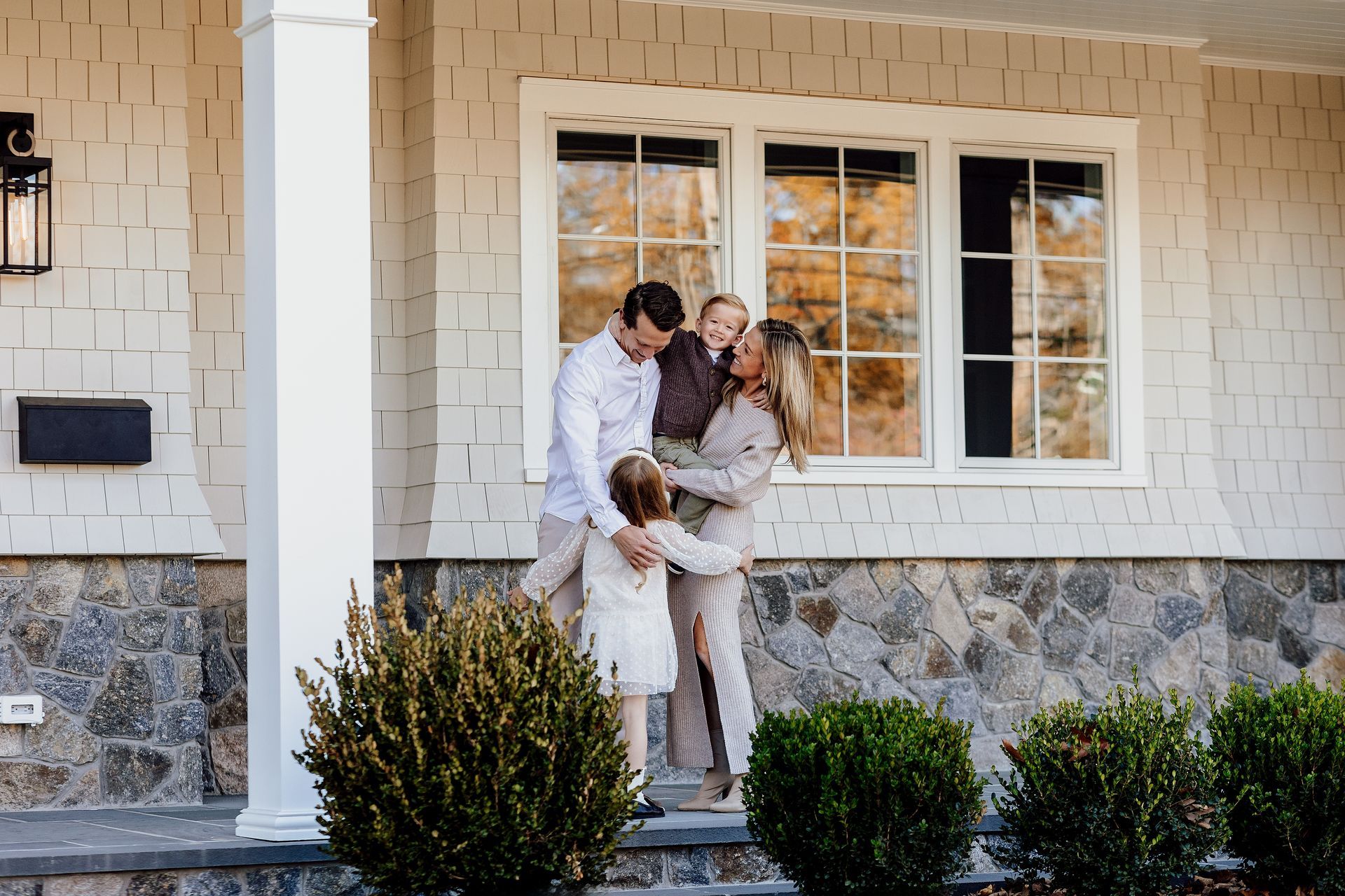 Family embraces in front of a house, two small children.