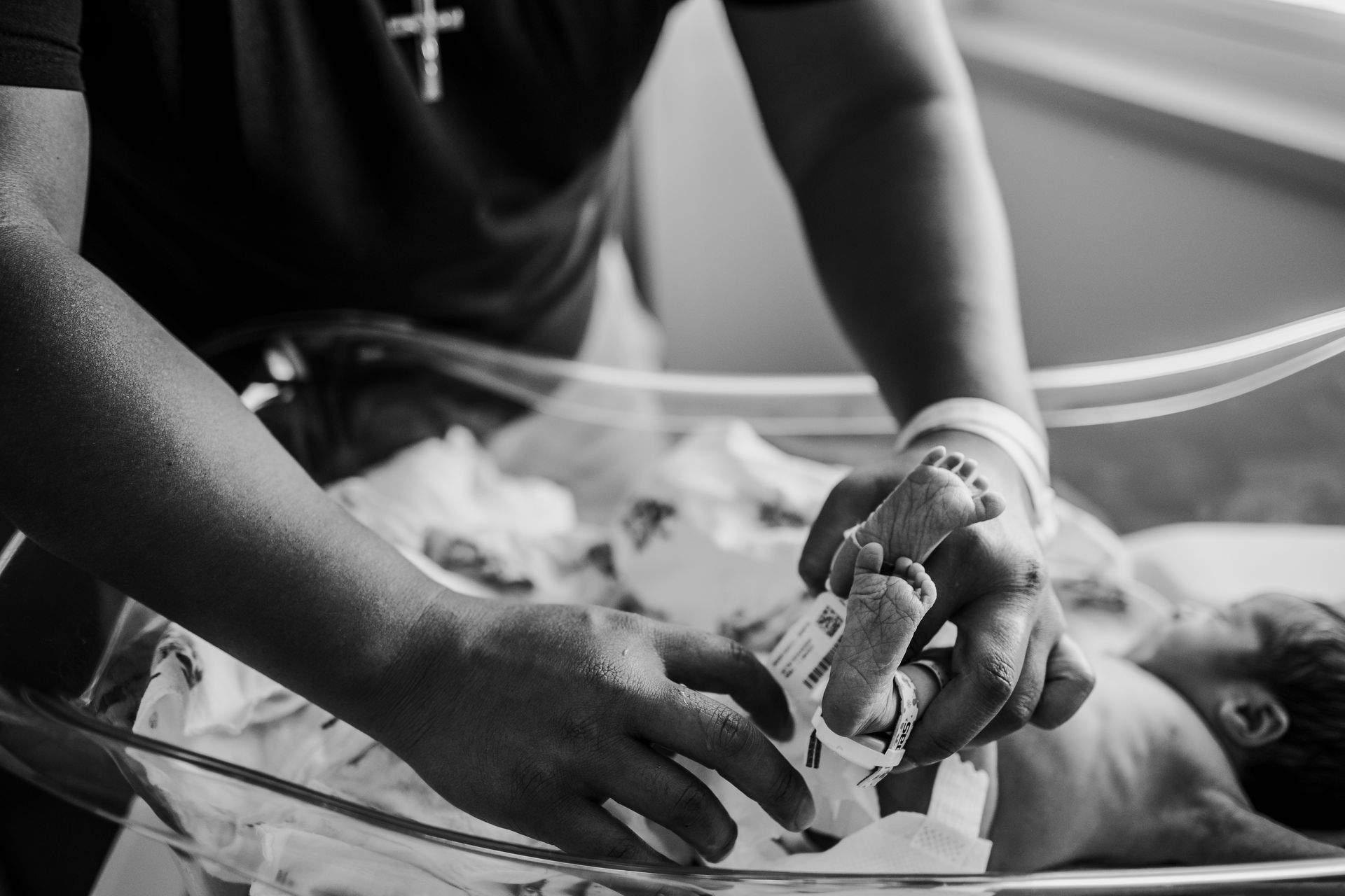 Person holding a newborn's feet in a hospital bassinet; black and white photo.