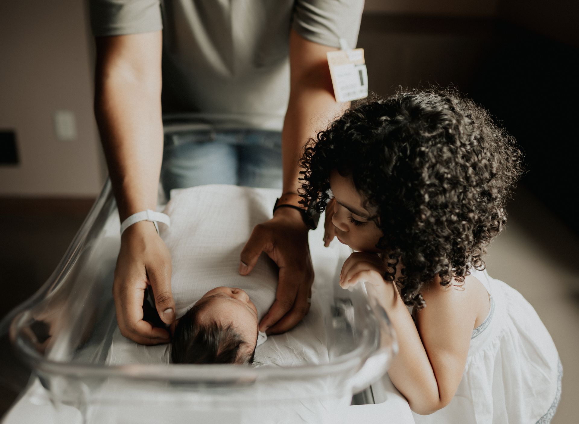 Father and child looking at newborn baby in hospital bassinet.