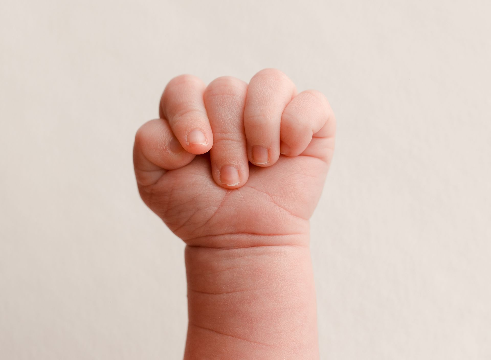 Baby's clenched fist, knuckles visible, against a light background.