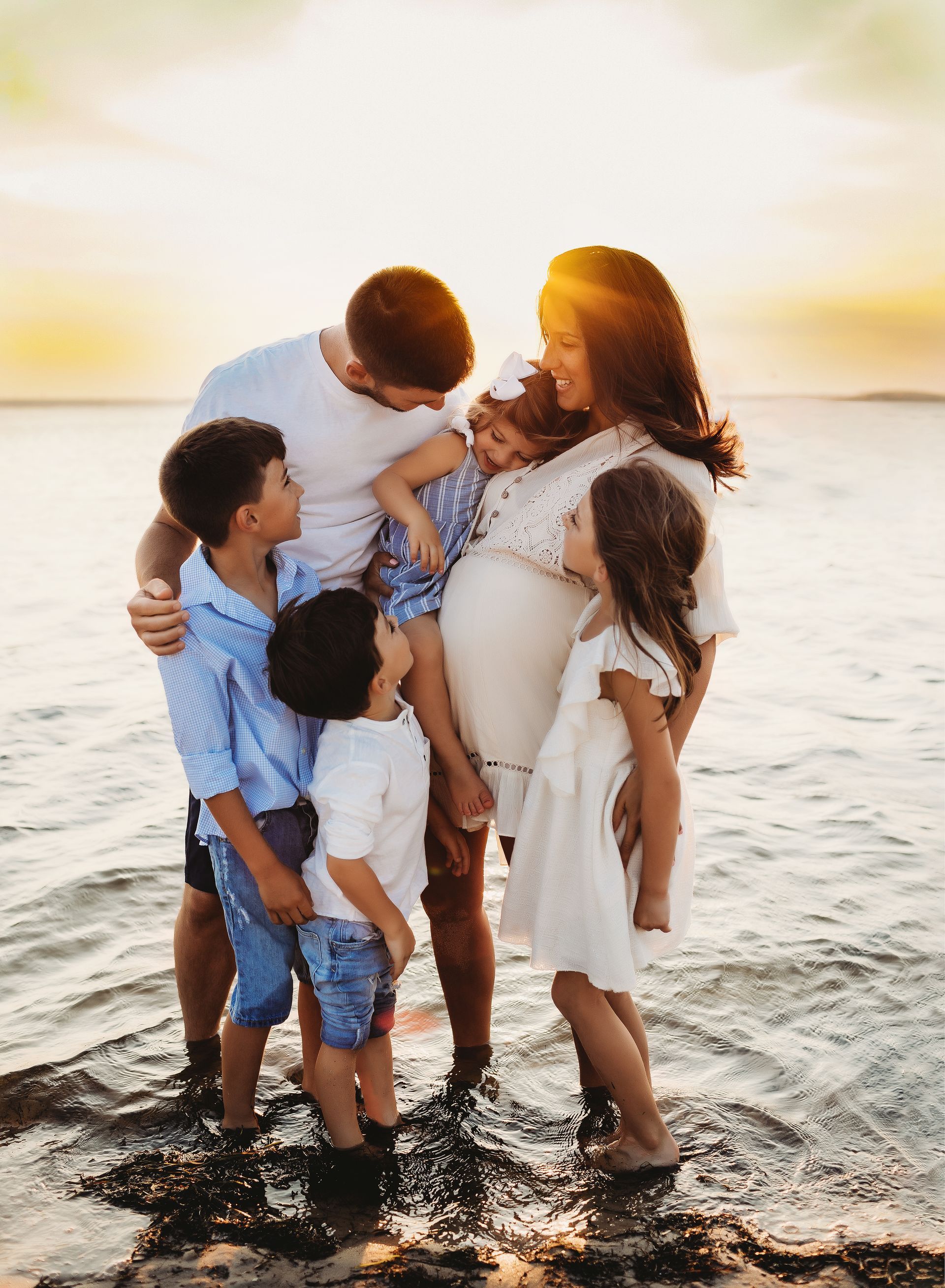Family of six in water, hugging, sunset in background.