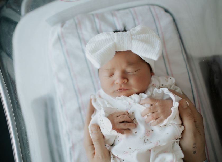 A person is holding a newborn baby in a hospital crib during a hospital photography session