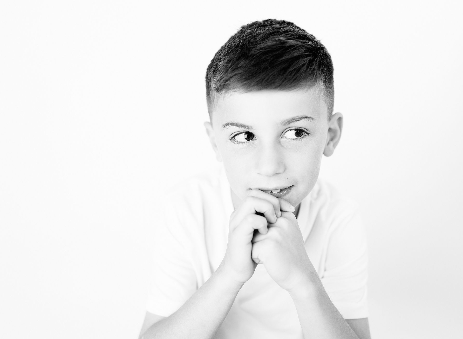 Boy with a thoughtful expression looking to the side, hands clasped, in black and white.