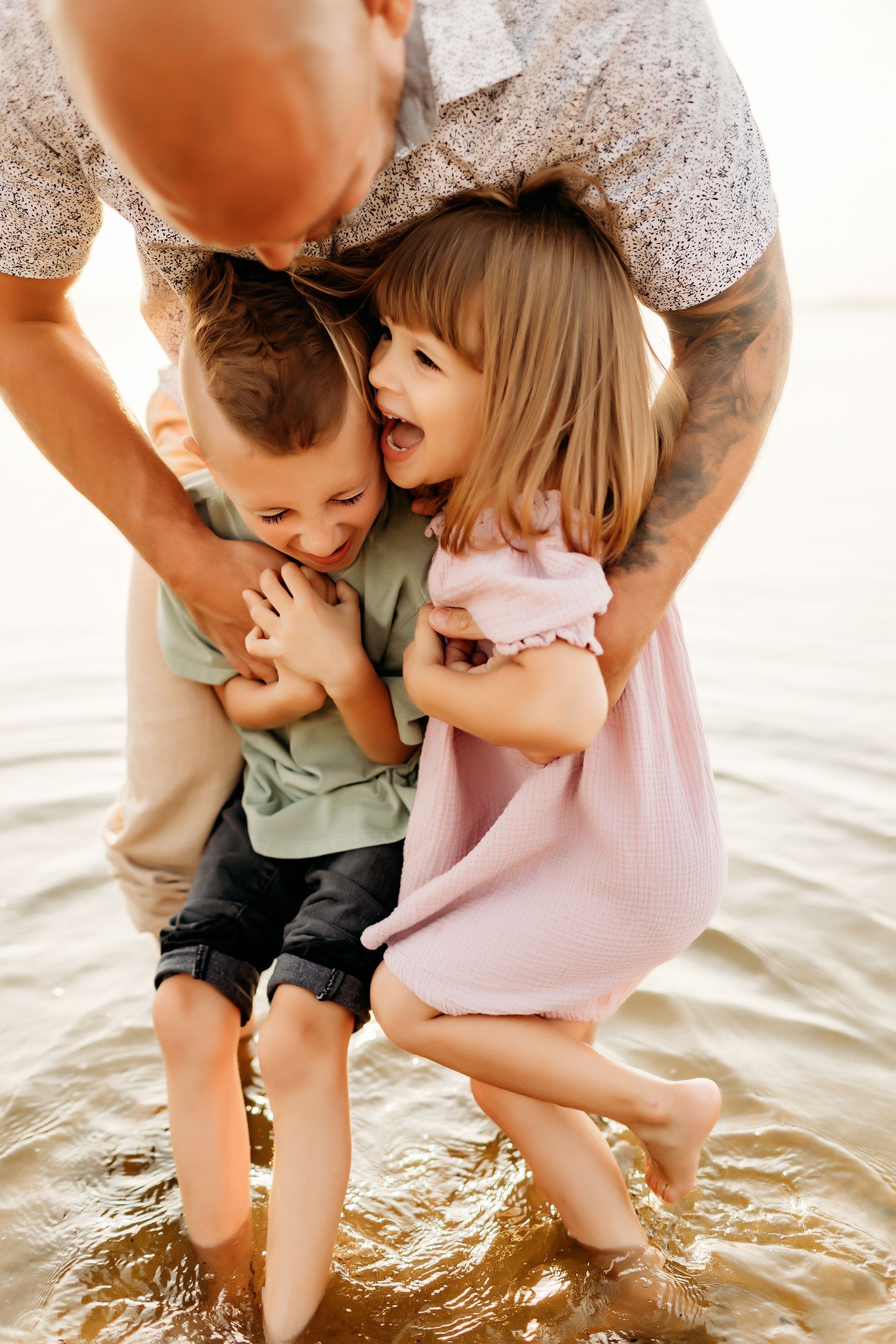 Man embracing two children in shallow water; joyful expressions.