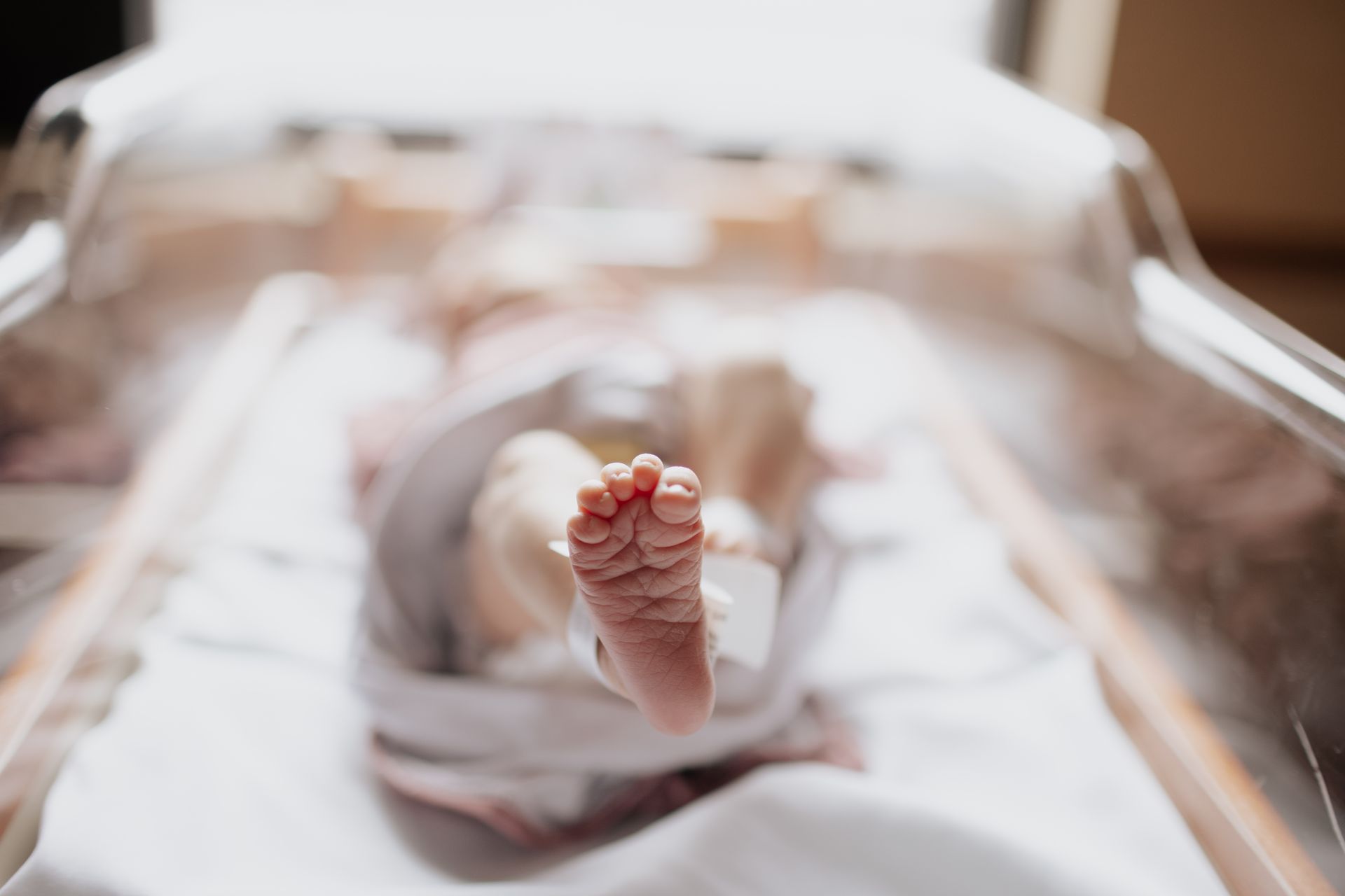 Baby's foot in focus, lying in a transparent hospital bassinet.