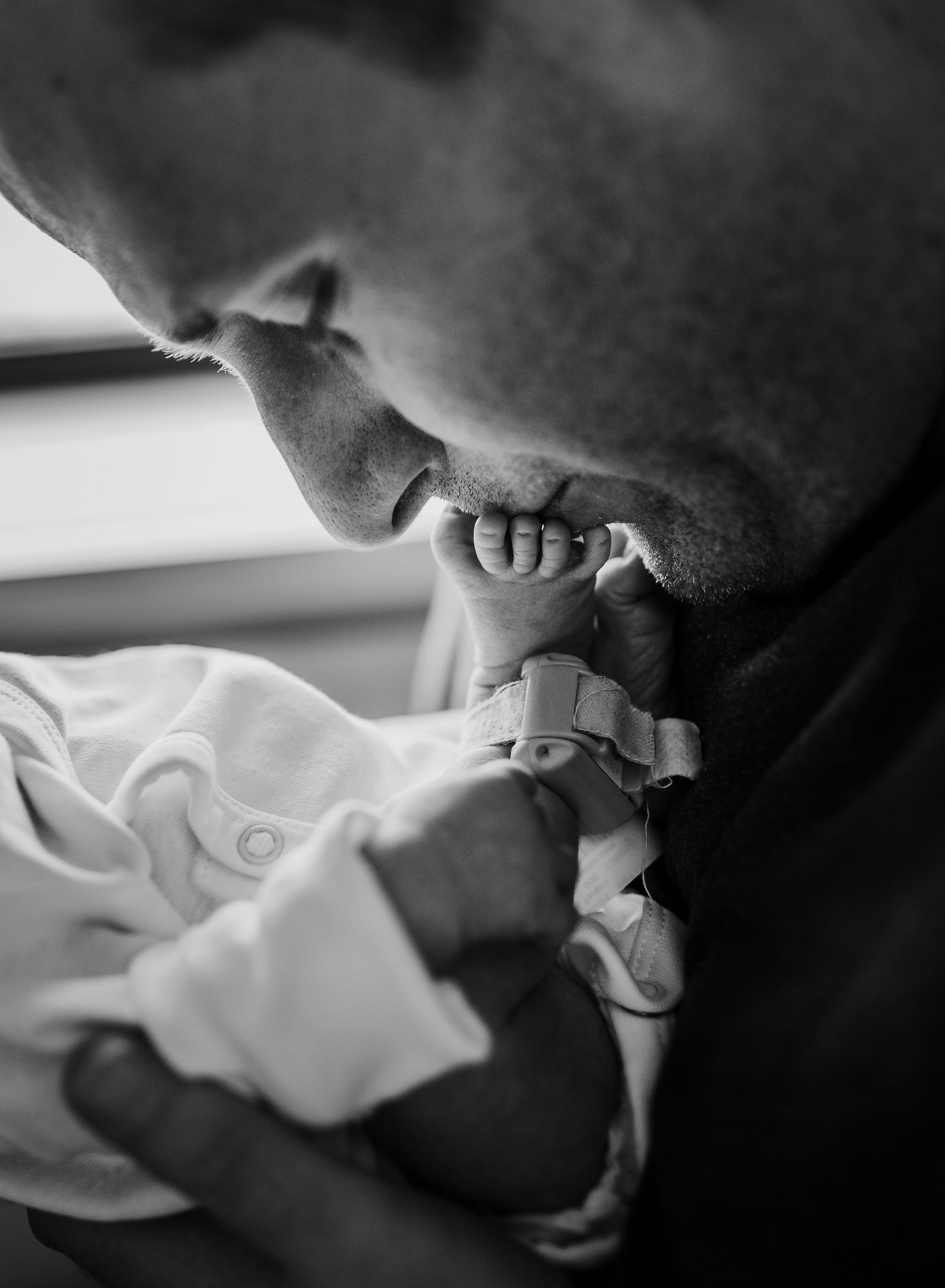 Man kissing a newborn's tiny foot. Black and white photo.