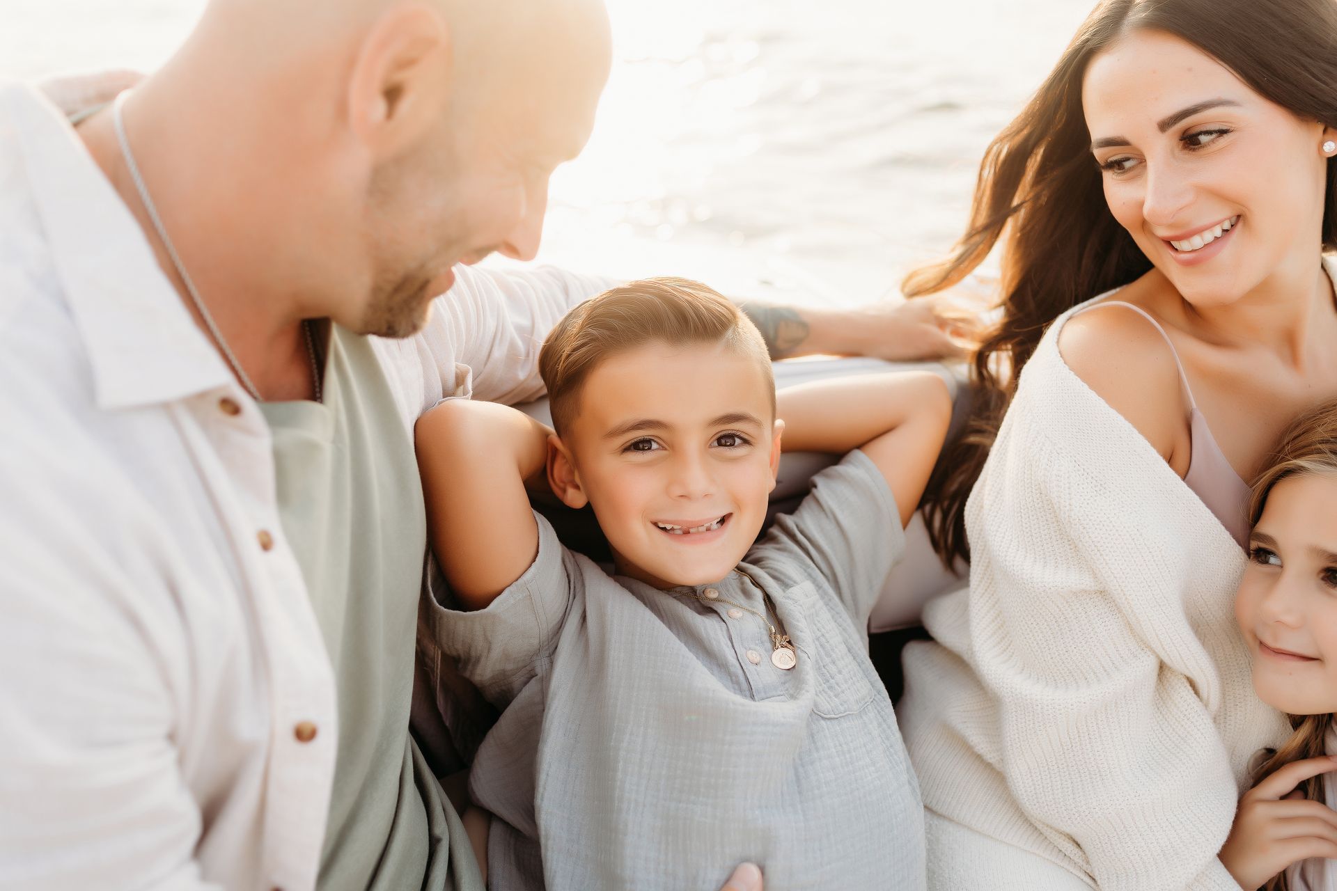 Family smiling outdoors; boy with hands behind head, sunny setting.