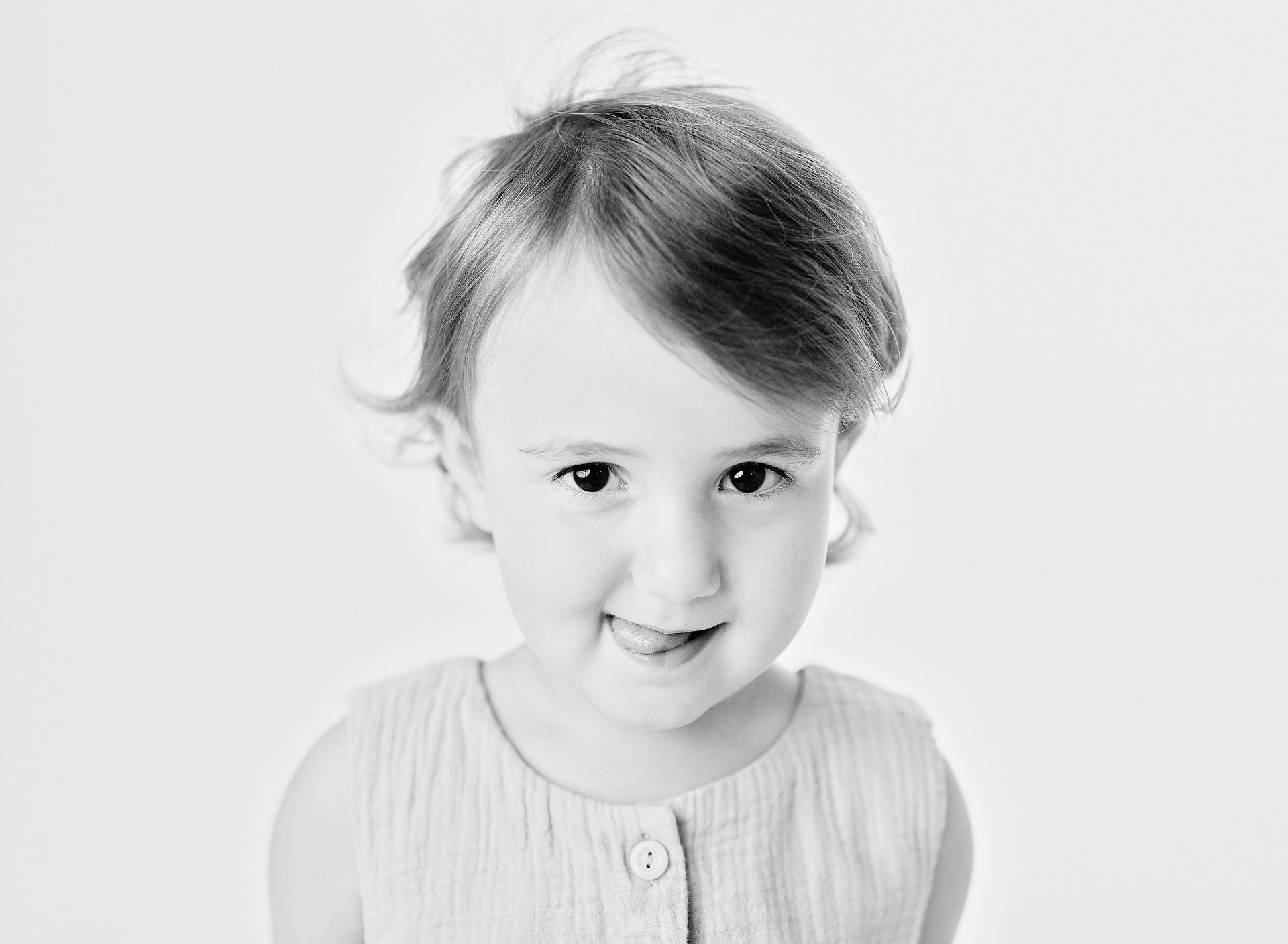 Young child with light skin, looking at the camera and smiling, wearing a sleeveless top.