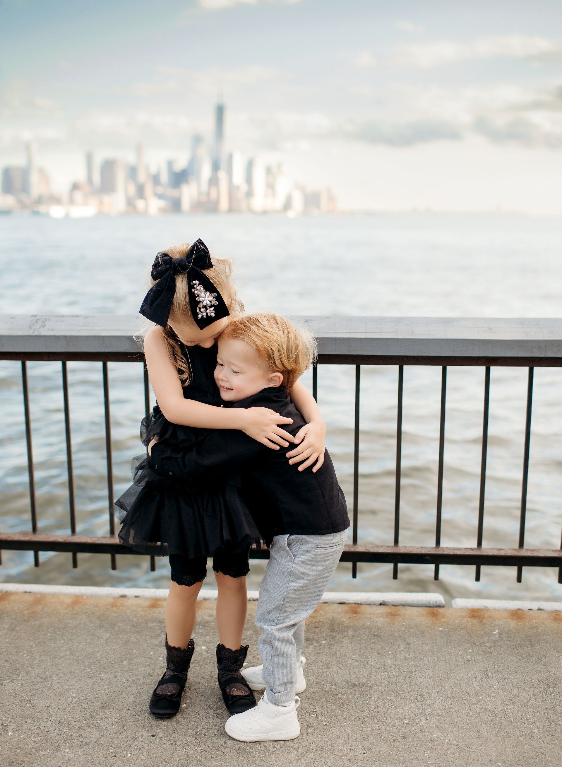A girl and a boy are hugging each other in front of a body of water.