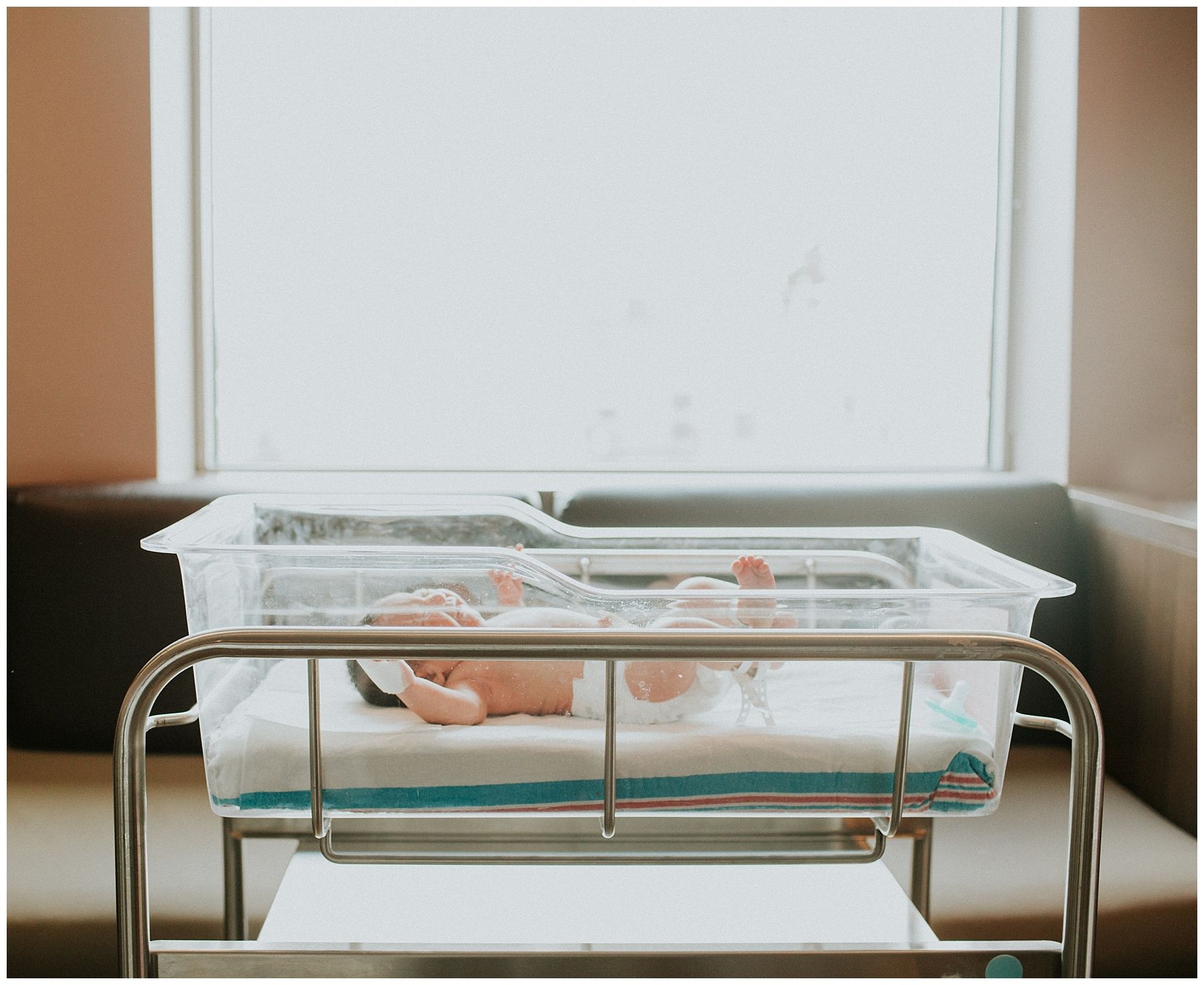 A baby is sleeping in a hospital bed in front of a window.