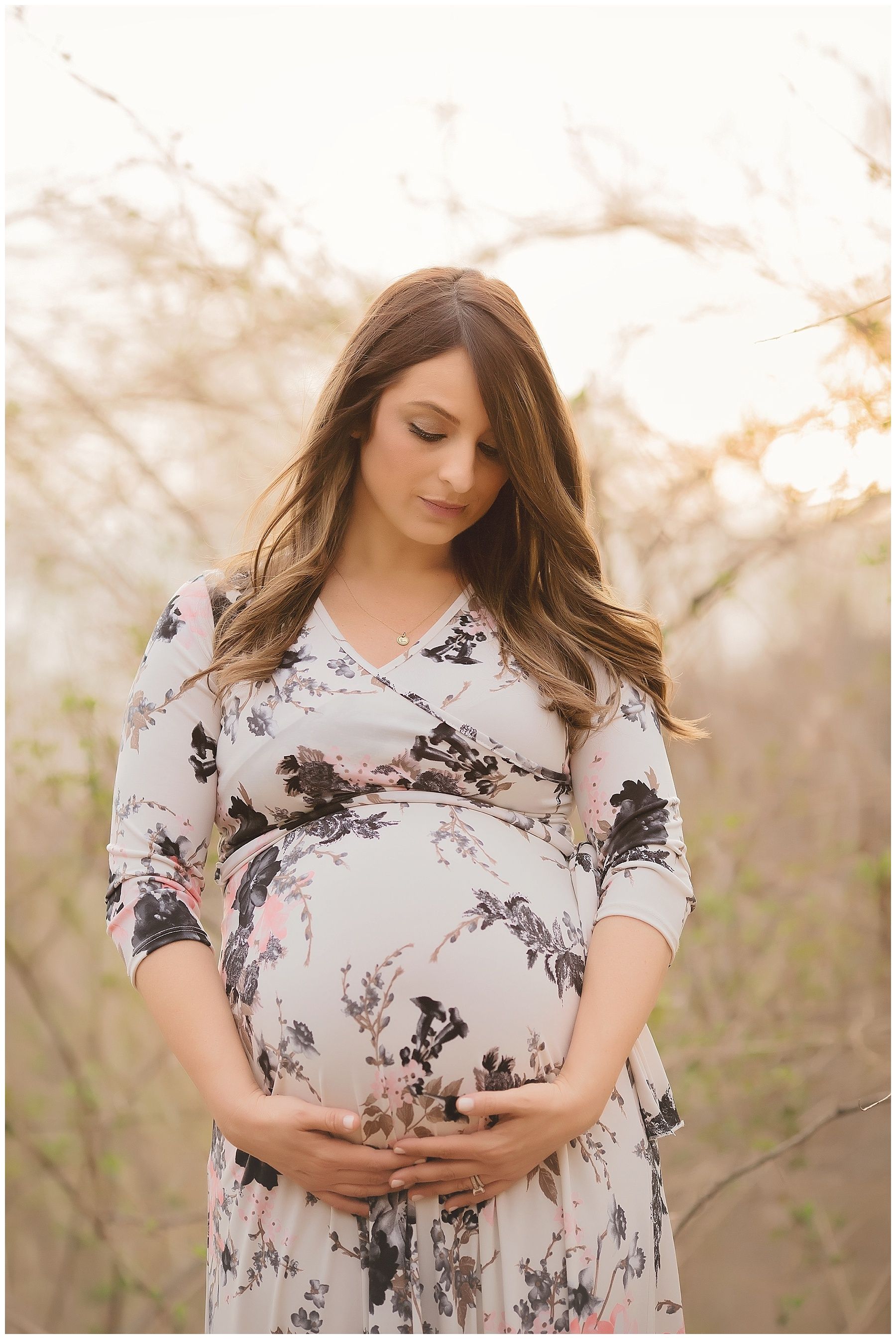 A pregnant woman in a floral dress is holding her belly.