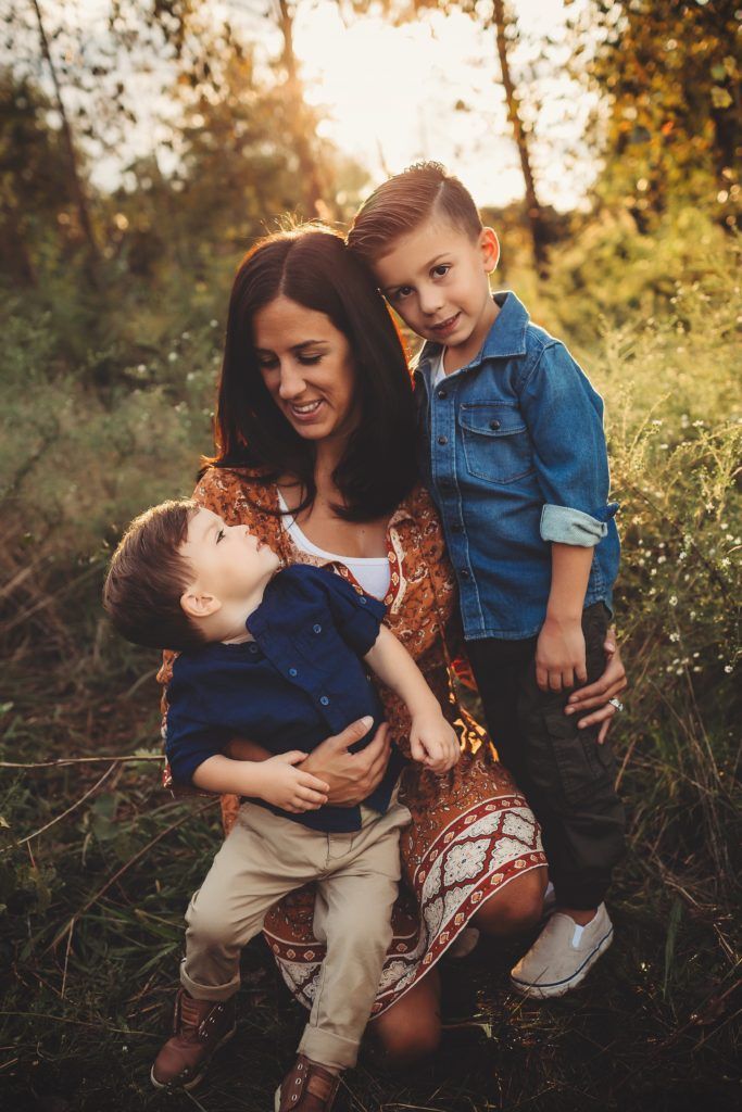 A woman is holding two children in her arms in a field.